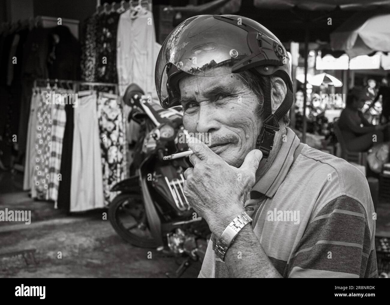 Un tassista del motociclo (xe om) fuma una sigaretta mentre attende i passeggeri fuori dal mercato centrale di Kontum, nelle Highlands centrali di Vietn Foto Stock