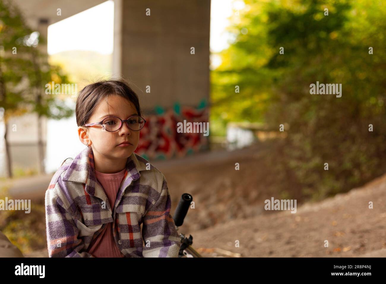 Graziosa bambina con occhiali seduti su una bicicletta nel parco Foto Stock