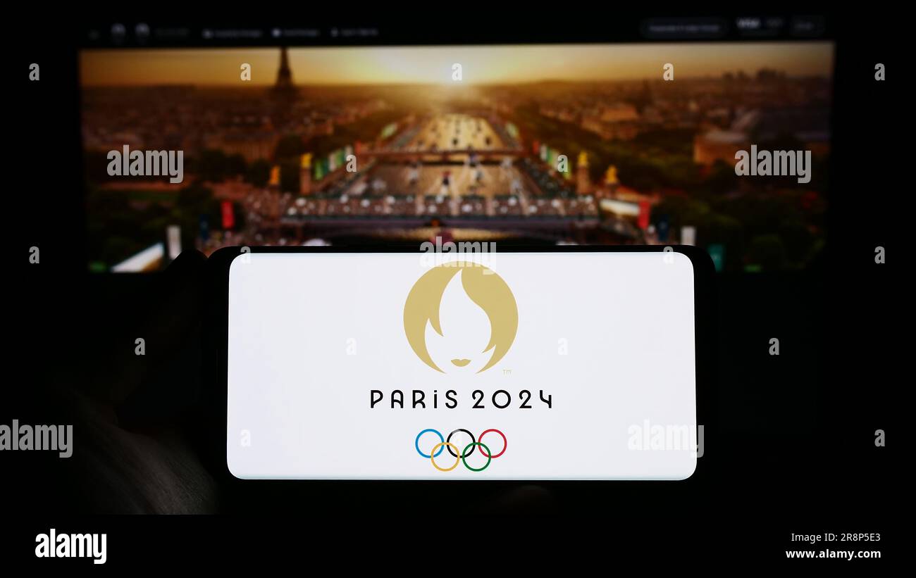 Persona che possiede uno smartphone con il logo delle Olimpiadi estive di Parigi del 2024 sullo schermo davanti al sito Web. Concentrarsi sul display del telefono. Foto Stock