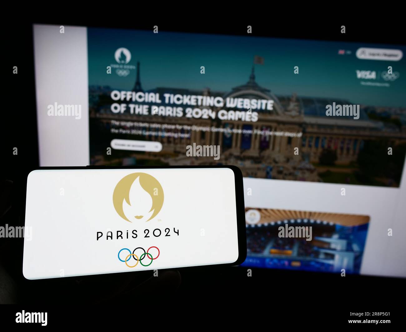 Persona che possiede il cellulare con il logo delle Olimpiadi estive di Parigi 2024 sullo schermo davanti alla pagina Web. Concentrarsi sul display del telefono. Foto Stock