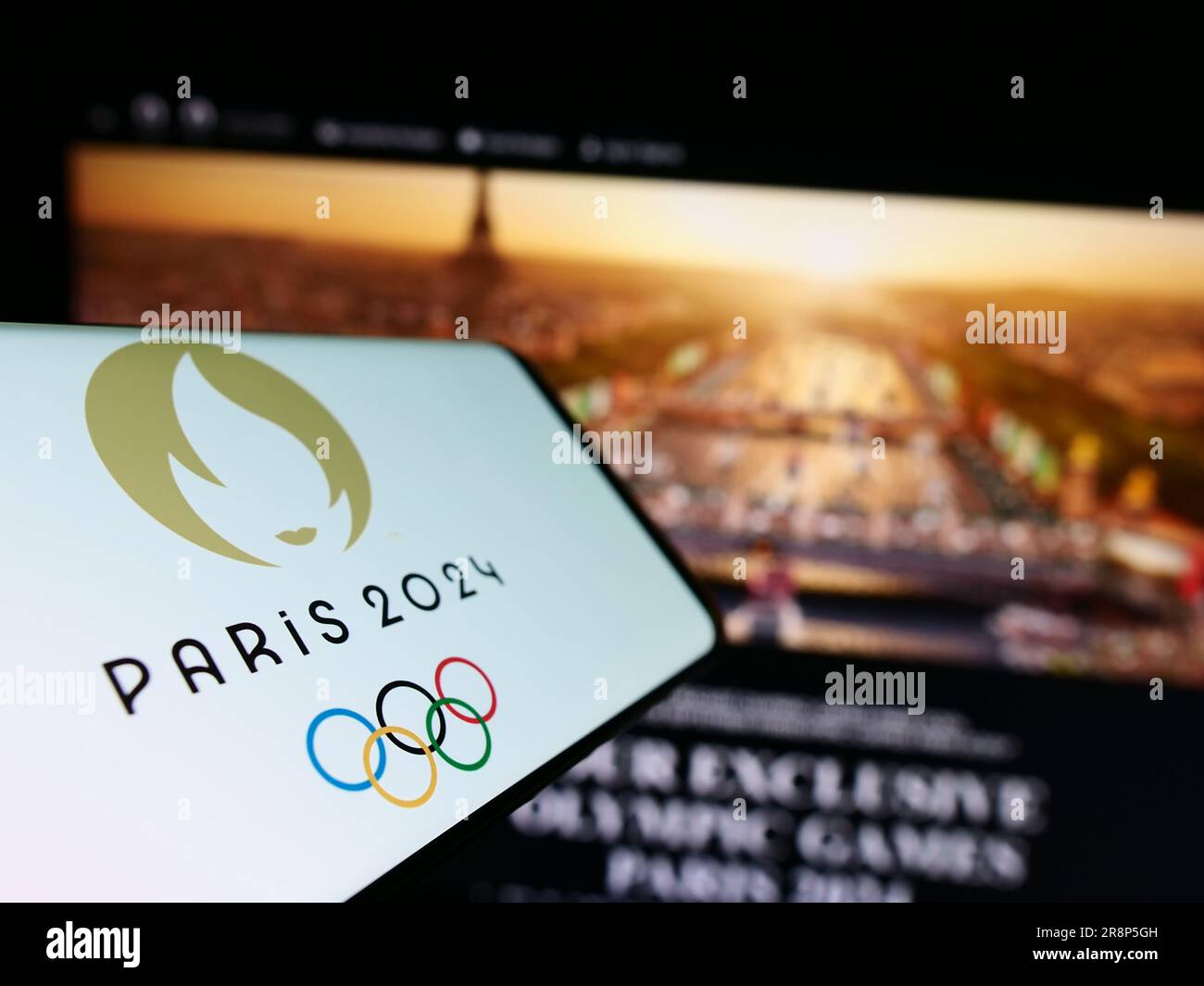 Cellulare con logo delle Olimpiadi estive di Parigi 2024 sullo schermo davanti al sito web. Mettere a fuoco il display centrale sinistro del telefono. Foto Stock