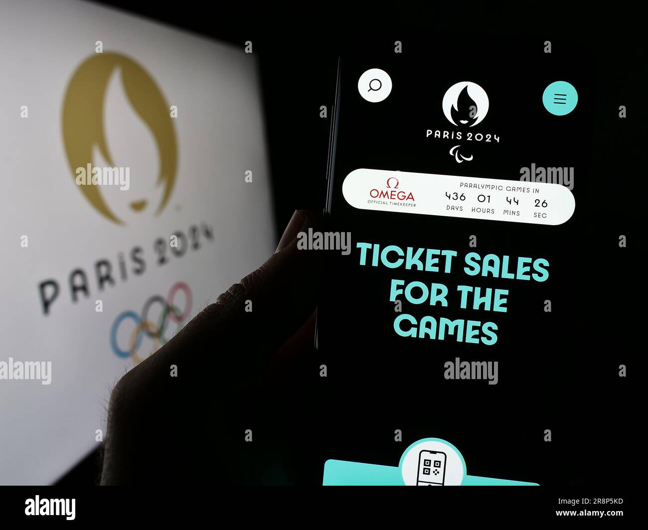 Persona che possiede il cellulare con una pagina Web delle Olimpiadi estive di Parigi 2024 sullo schermo davanti al logo. Concentrarsi sul centro del display del telefono. Foto Stock