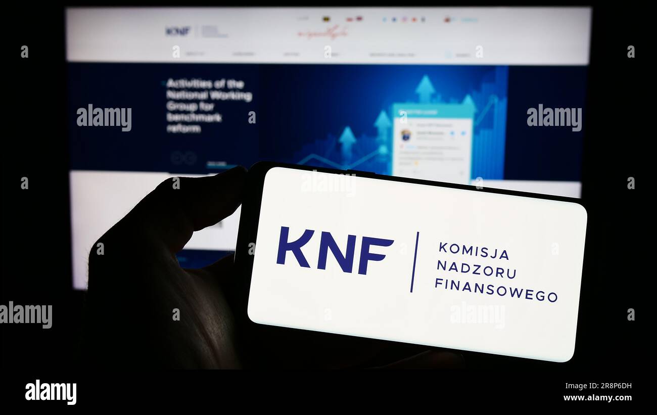 Persona in possesso di un cellulare con il logo dell'autorità Komisja Nadzoru Finansowego (KNF) sullo schermo di fronte alla pagina web. Concentrarsi sul display del telefono. Foto Stock