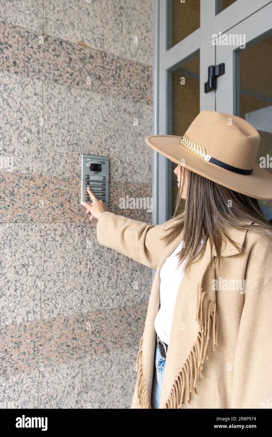 Una giovane donna che indossa un cappello beige sta davanti ad una porta aperta, guardando all'interno con curiosità Foto Stock