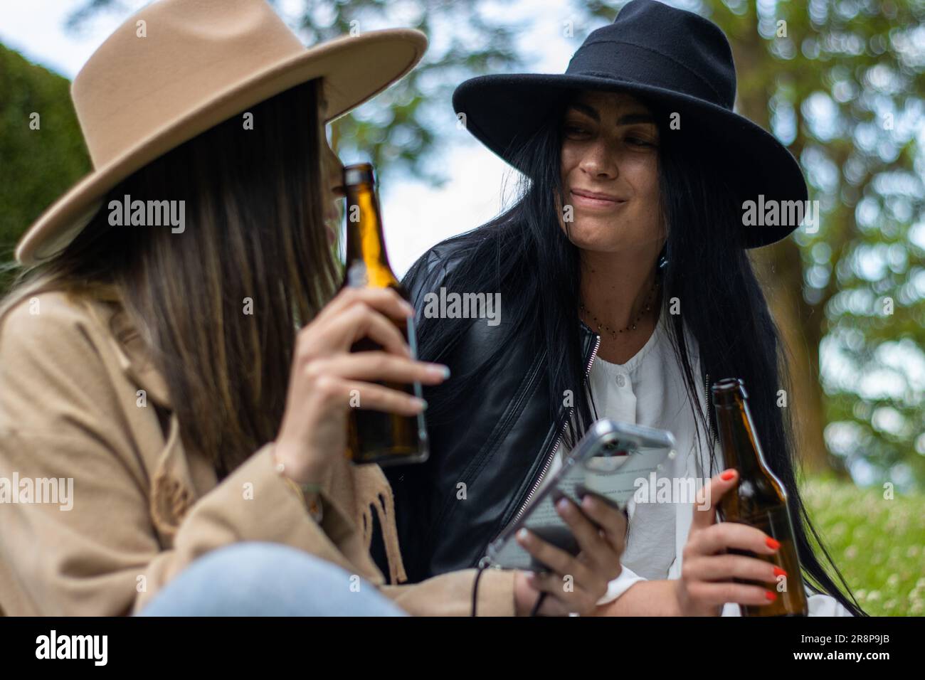 Due amici sorridono e gustano una birra insieme all'aperto in un parco Foto Stock