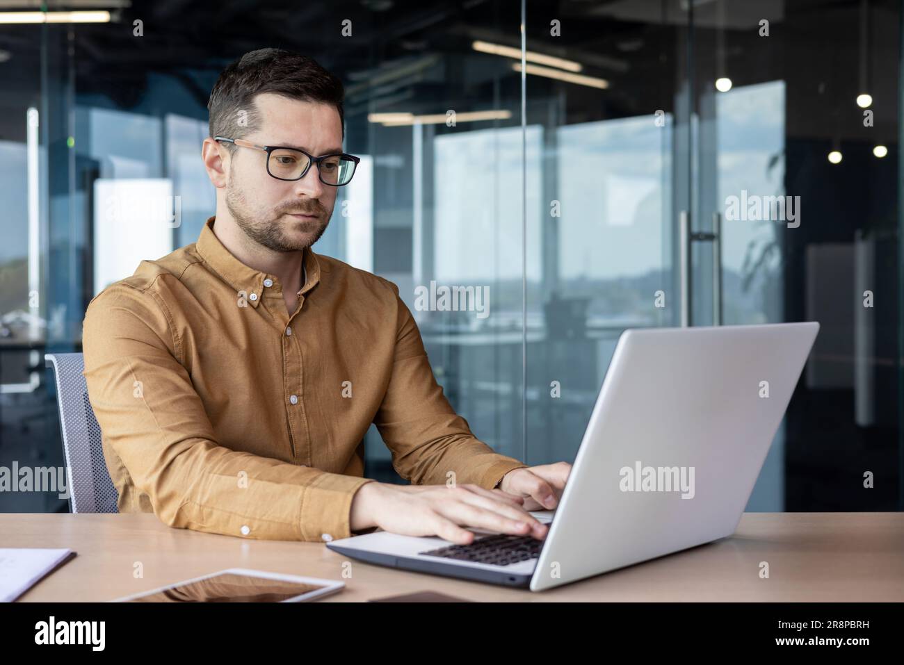 Ritratto di un giovane e serio programmatore, sviluppatore specializzato che si sta concentrando sul lavoro su un computer portatile mentre si è seduti alla scrivania in un centro ufficio. Foto Stock