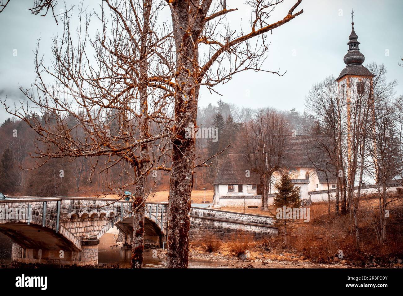 Un vecchio ponte di pietra si erge su un tranquillo fiume, con una vecchia torre che sorge sullo sfondo Foto Stock