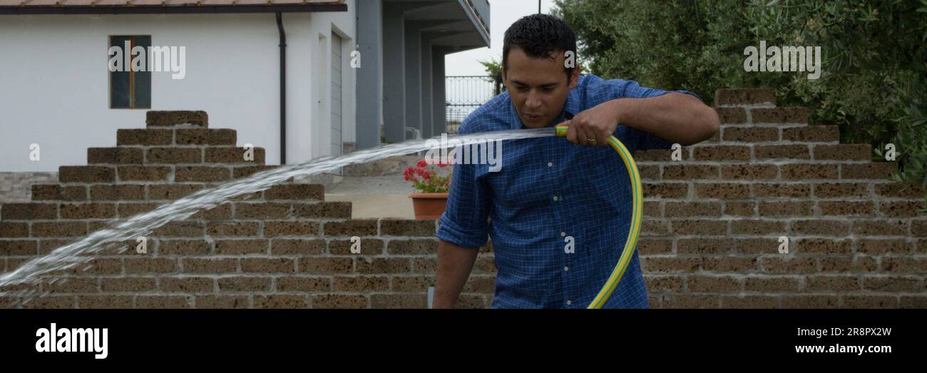 Immagine di un uomo nel suo giardino di casa che beve acqua da un tubo per prato. Riferimento ai rifiuti idrici. Striscione orizzontale Foto Stock