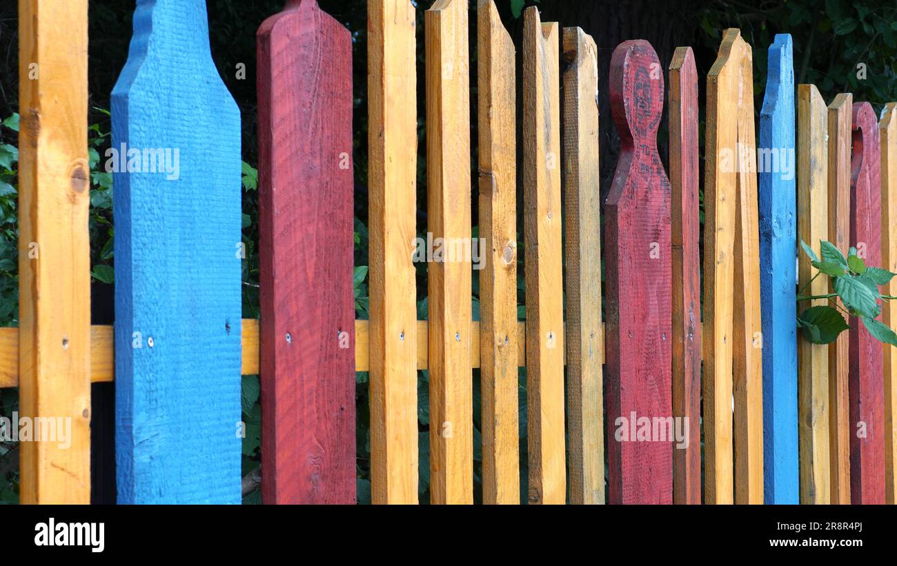 Una colorata recinzione in giardino di giallo, blu e rosso. Foto Stock