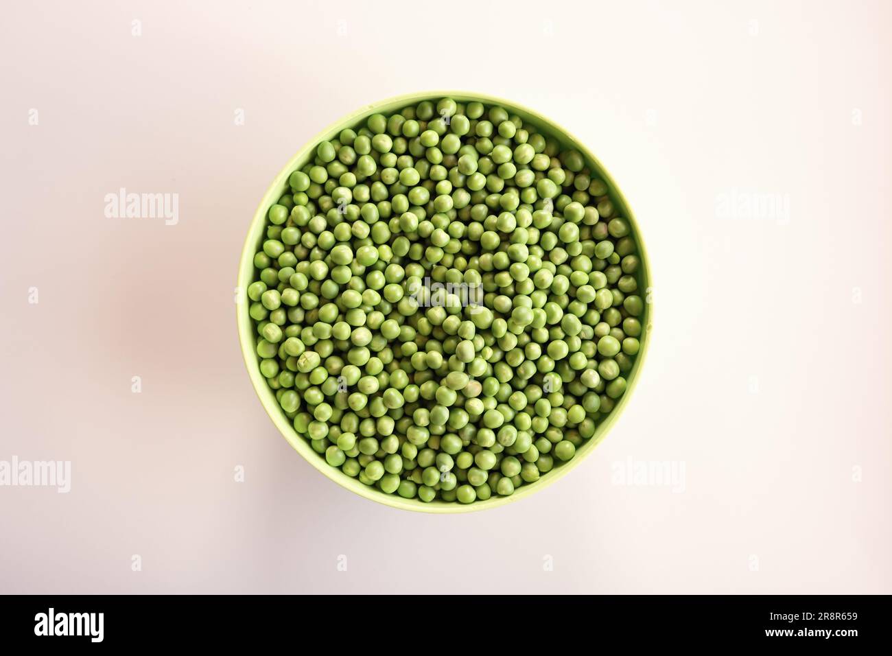 Piselli verdi freschi in una ciotola verde isolata su bianco. Vista dall'alto. Foto Stock