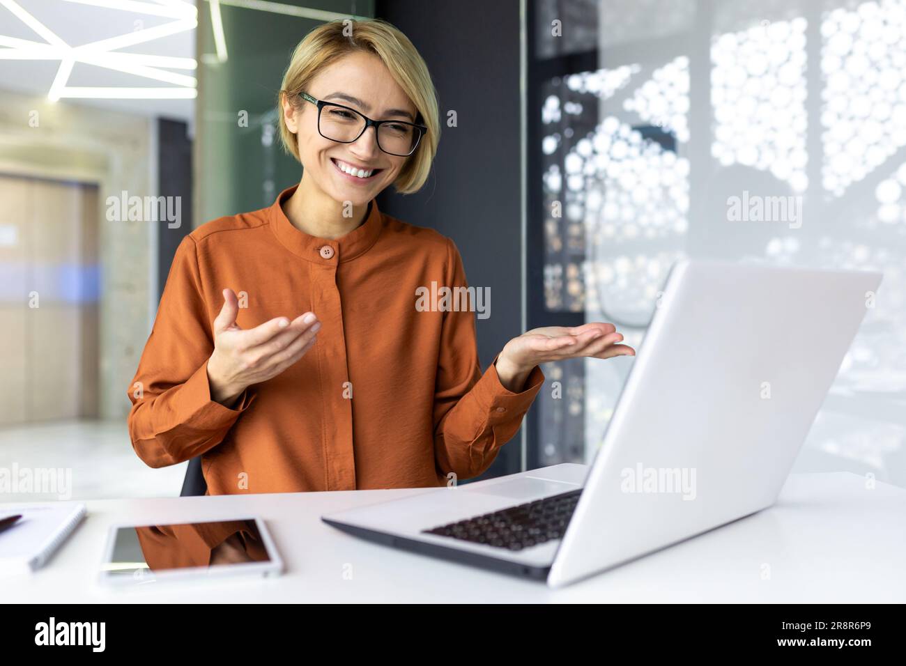 Donna d'affari felice che lavora in un ufficio moderno utilizzando un computer portatile per videochiamate e riunioni online con altri dipendenti, donna sorridente e divertente per una presentazione. Foto Stock
