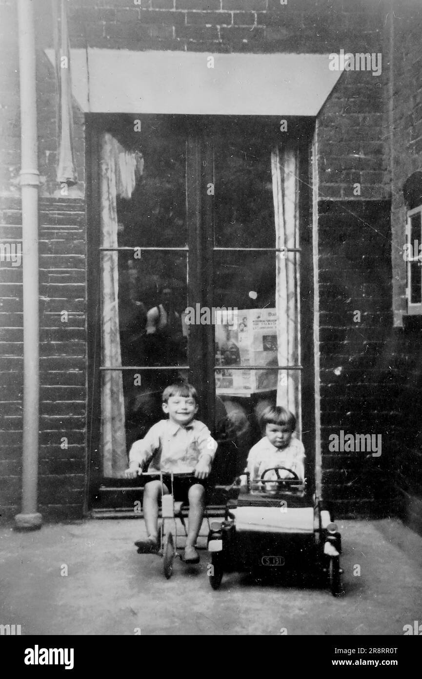 Due bambini, una bambina in un'auto giocattolo e un bambino su un triciclo, fuori da una porta d'ingresso. Si tratta di una fotografia tratta da un album di scatti principalmente istantanee, c1929, durante l'occupazione della Palestina da parte dell'esercito britannico, con foto dalla Palestina e dal Regno Unito tra cui devil's Jump vicino a Churt nel Surrey e devil's Punch Bowl. L'addestramento sembra essere a Hursley Camp, vicino a Winchester. La Gran Bretagna amministrò la Palestina per conto della società delle Nazioni tra il 1920 e il 1948, un periodo denominato "mandato britannico”. Foto Stock