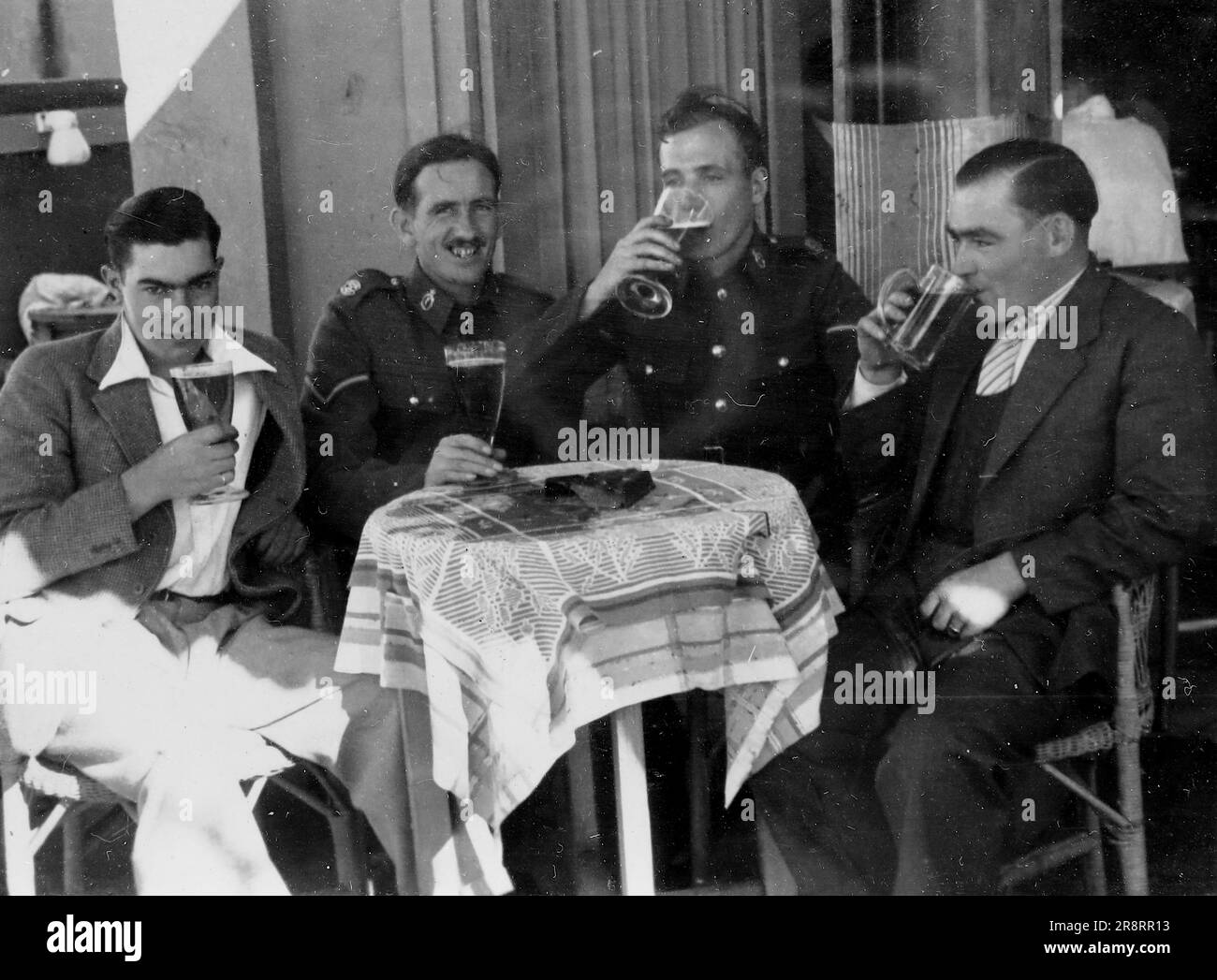 Un gruppo di quattro uomini seduti intorno a un piccolo tavolo che beve. Due indossano le uniformi dell'esercito britannico. Palestina, c1930. Si tratta di una fotografia tratta da un album di scatti, durante l'occupazione della Palestina da parte dell'esercito britannico, con foto provenienti dalla Palestina e dal Regno Unito, tra cui devil's Jump vicino a Churt nel Surrey e devil's Punch Bowl. L'addestramento sembra essere a Hursley Camp, vicino a Winchester. La Gran Bretagna amministrò la Palestina per conto della società delle Nazioni tra il 1920 e il 1948, un periodo denominato "mandato britannico”. Foto Stock