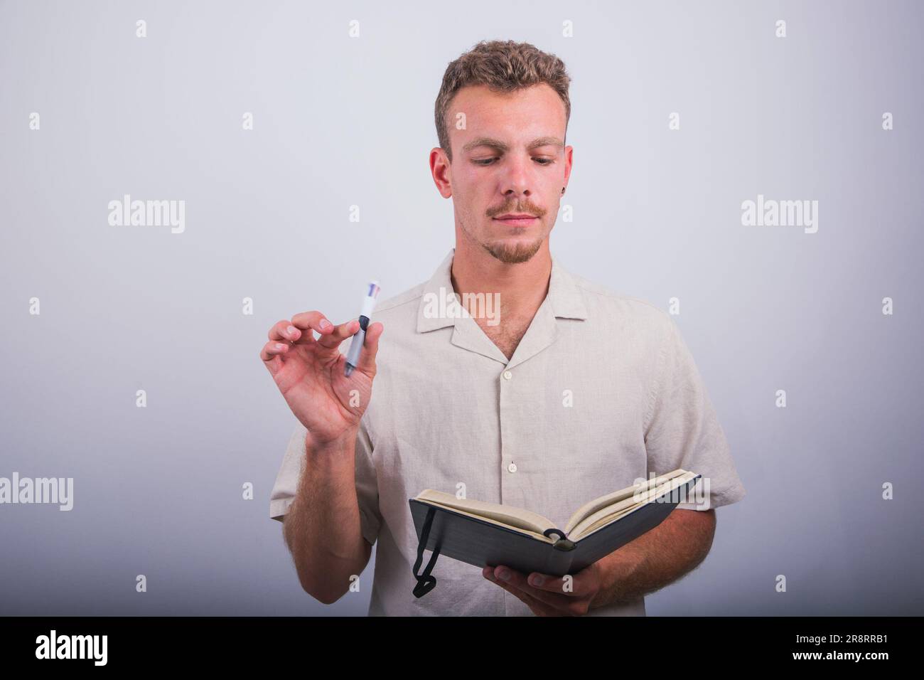 Uno scrittore tiene in mano una penna e un libro e cerca ispirazione per scrivere Foto Stock