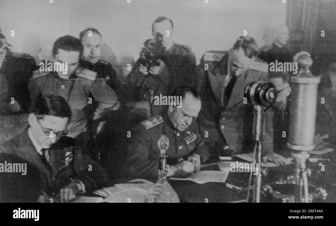 Gli ufficiali alleati firmano i termini di rinuncia di Berlino -- Il capo dell'aviazione britannico Sir Arthur Tedder (seduto, a sinistra), vice comandante supremo delle forze alleate occidentali e il capo russo Gregory K. Zhukov (seduto a destra), vice comandante di tutte le forze sovietiche, firmano i termini di resa incondizionati imposti ai tedeschi a Berlino il 9 maggio. Altri in background non identificati. 10 maggio 1945. (Foto di Radiophoto Press associato). Foto Stock