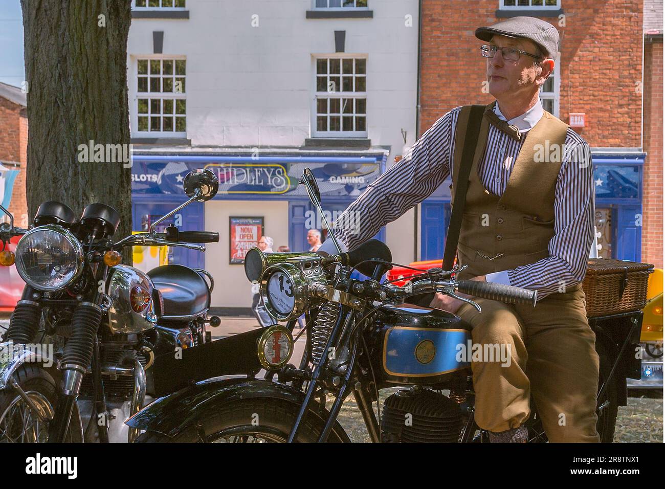 Un ritratto dell'orgoglioso proprietario di una motocicletta Triumph Model NSD in piedi accanto alla sua motocicletta mentre indossa un costume d'epoca. Moto d'epoca. Foto Stock