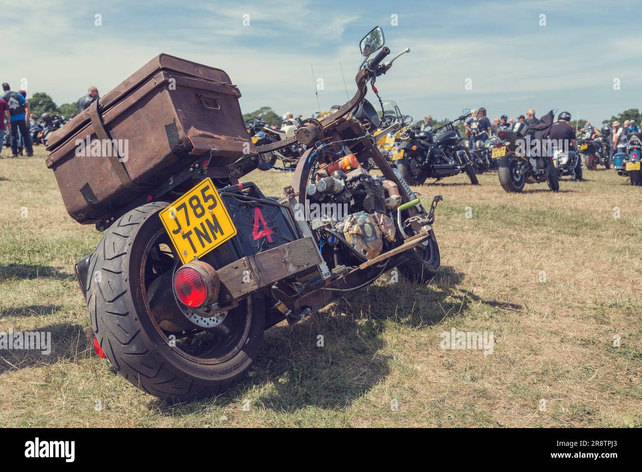 File di motociclette allineate a un motociclista si incontrano. In primo piano c'è una moto arrugginita fatta in casa costruita intorno a un motore Suzuki. Foto Stock