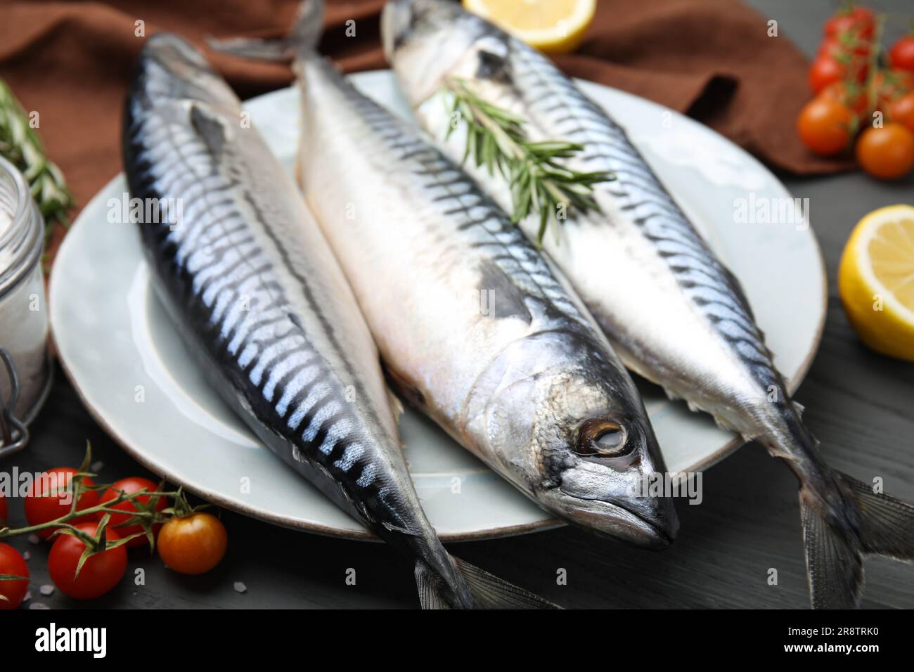 Sgombro crudo, pomodori e rosmarino su tavola di legno nero, primo piano Foto Stock