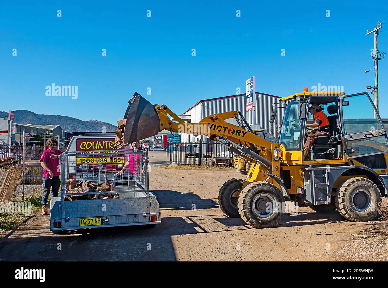 Caricatore frontale giallo che colloca legna da incendio nel rimorchio del cliente. Tamworth Australia. Foto Stock