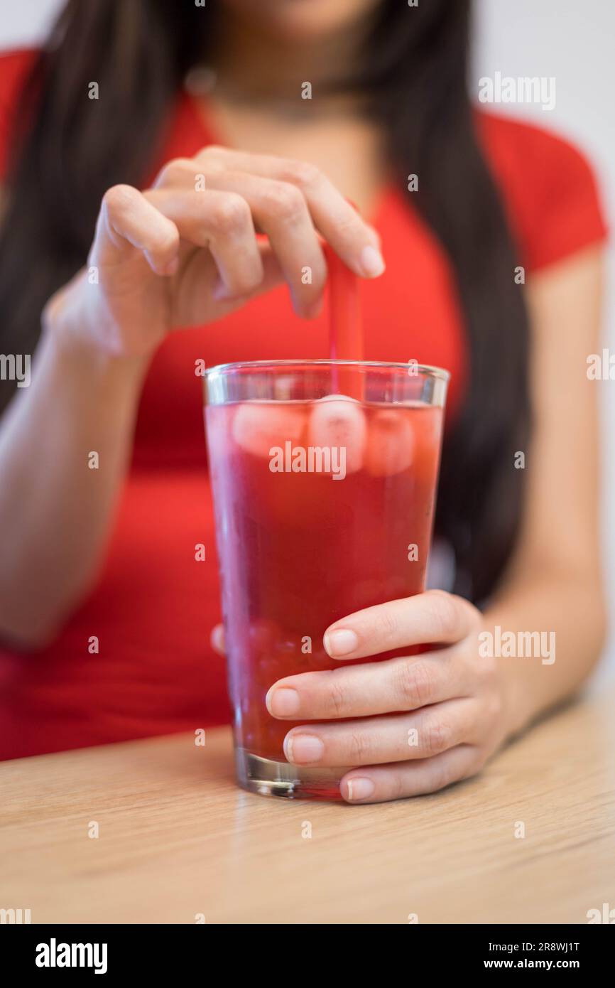tenendo un bicchiere di cristallo con tè alla frutta rossa ghiacciata, una deliziosa bevanda rinfrescante con ghiaccio e paglia, uno stile di vita rilassante gustando un drink, ristorante Foto Stock