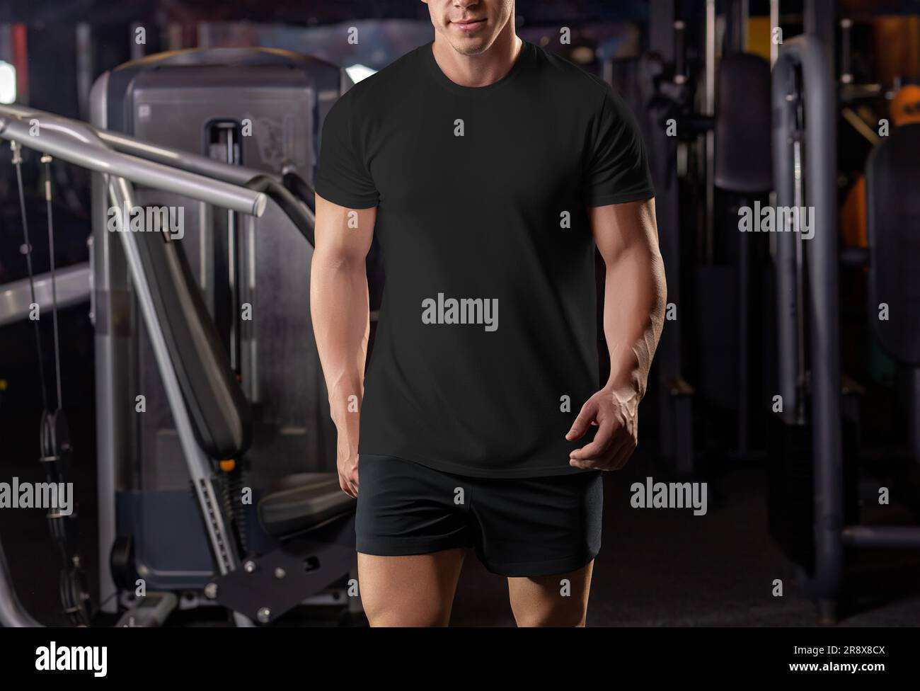 Modello di t-shirt nera su un uomo muscoloso che cammina in palestra, dalla testa alle ginocchia, dall'abbigliamento sportivo alla vista frontale. Modello di camicia su un atleta muscoloso, per il design Foto Stock