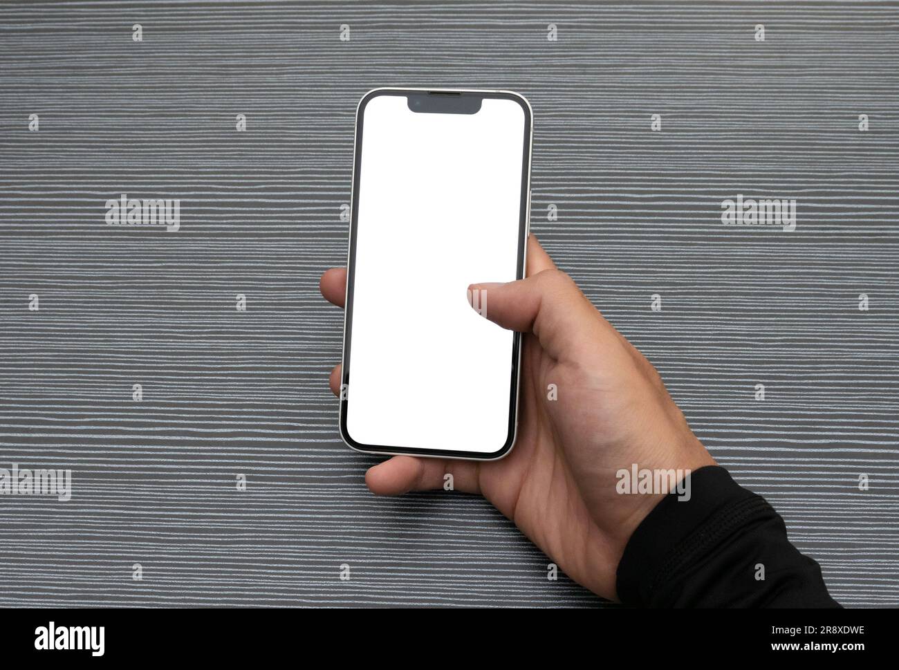 Concept per brochure e pubblicità. Mano che regge un telefono con display bianco su sfondo testurizzato del tavolo. Foto Stock