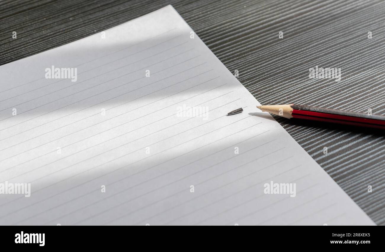 Matita rotta e carta bianca su un tavolo in legno testurizzato con ombre parziali, dopo alcune modifiche. Foto Stock