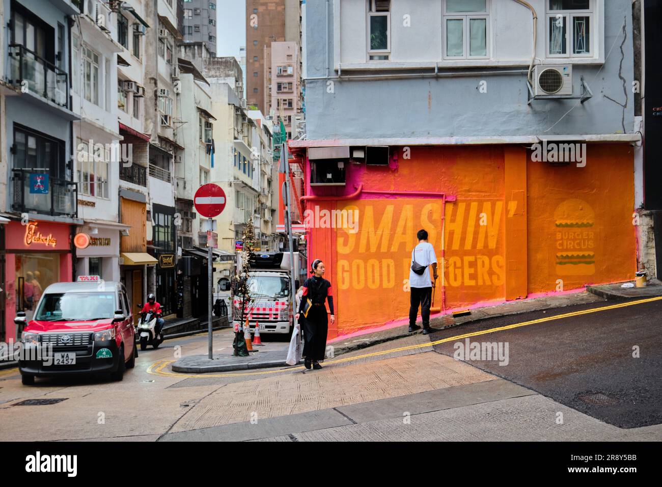Hong Kong, Cina - 24 aprile 2023: Un uomo che dipinge il muro di colore arancione per coprire i segni degli hamburger nel centro Foto Stock