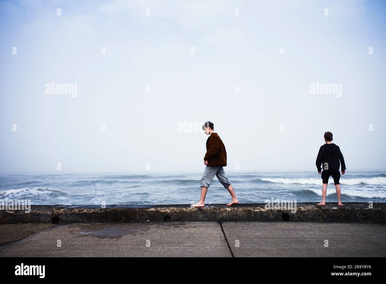 I giovani adolescenti camminano lungo il muro di mare con l'alta marea a Scarborough Foto Stock