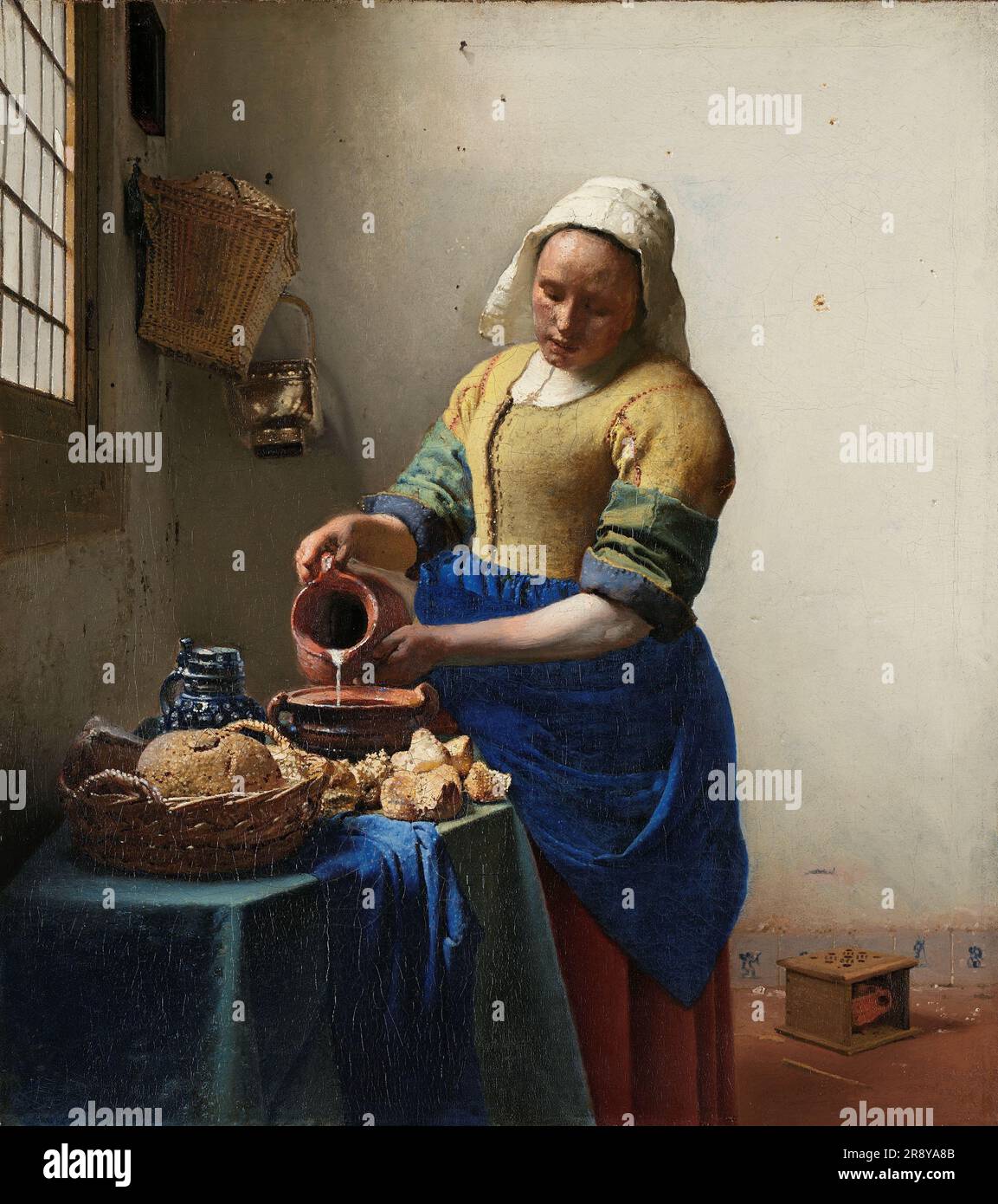 La Milkmaid, c.1660. Una cameriera si concentra molto mentre versa il latte da una brocca. E' una scena tranquilla e tranquilla. L'unico movimento è il flusso di latte. Vermeer ha trasformato una semplice composizione di un soggetto prosaico in un'intensa opera d'arte. È nel rendering della luce che Vermeer ha veramente eccelluto, dipingendo piccoli puntini per i punti salienti, come sul pane e sul panno blu. Foto Stock