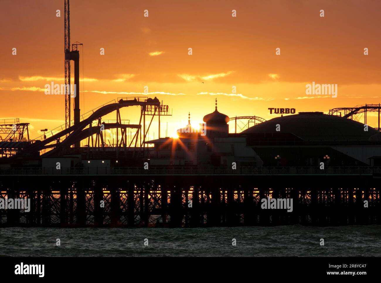 Il sole serale tramonta dietro due cupole a cipolla alla fine del molo del Palazzo di Brighton. Foto Stock