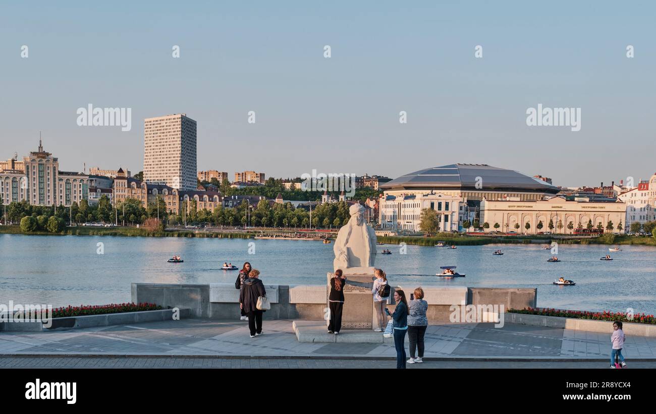 Kazan, Russia - 5 giugno 2023: Paesaggio urbano estivo. I turisti si trovano nei pressi del monumento all'educatore tataro Marjani sull'argine del lago Nizhny Kaban. Gente che cavalca catama Foto Stock