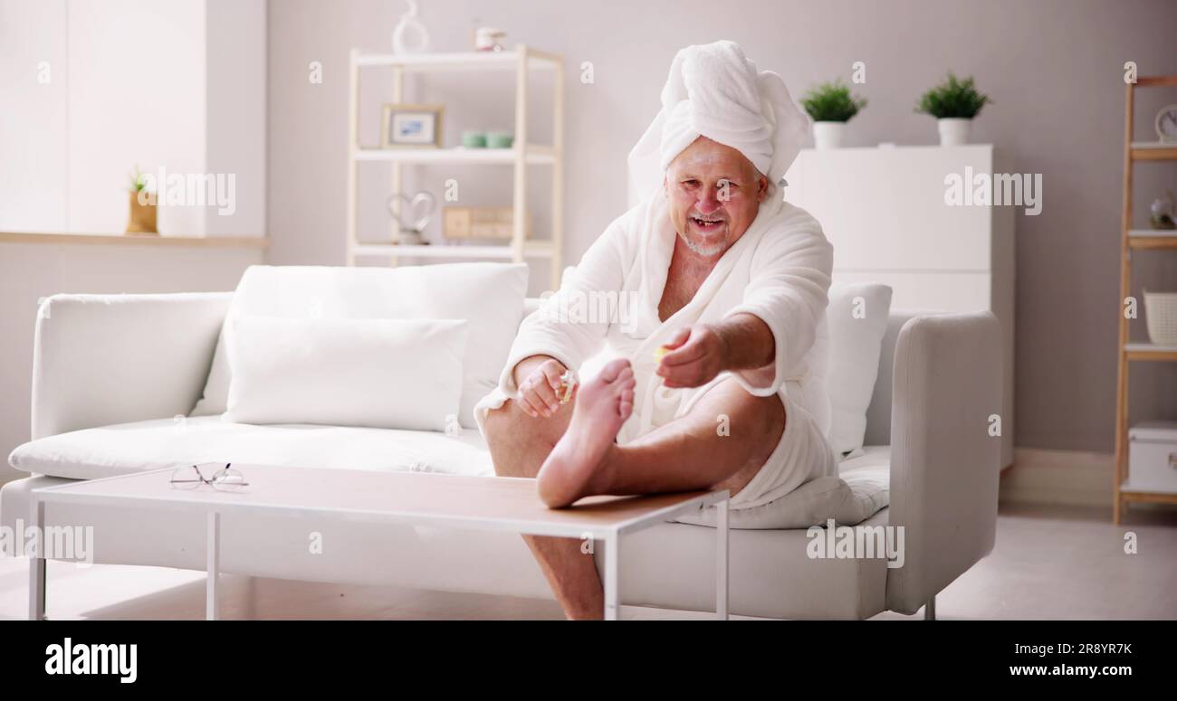 Divertente uomo che si rilassa in accappatoio facendo pedicure Spa a casa Foto Stock