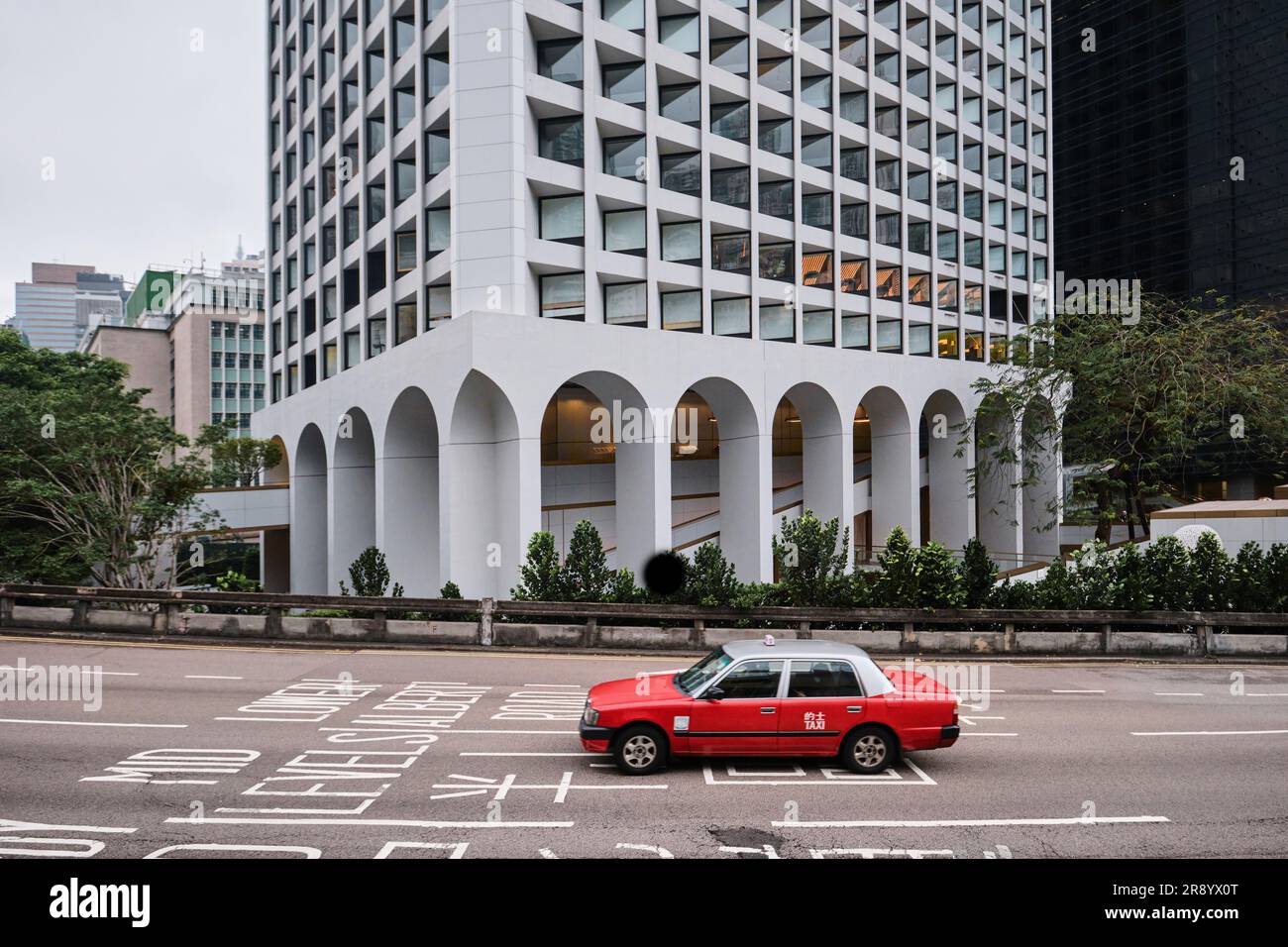 Hong Kong, Cina - 24 aprile 2023: The Murray Hotel, con un taxi rosso che passa in primo piano Foto Stock