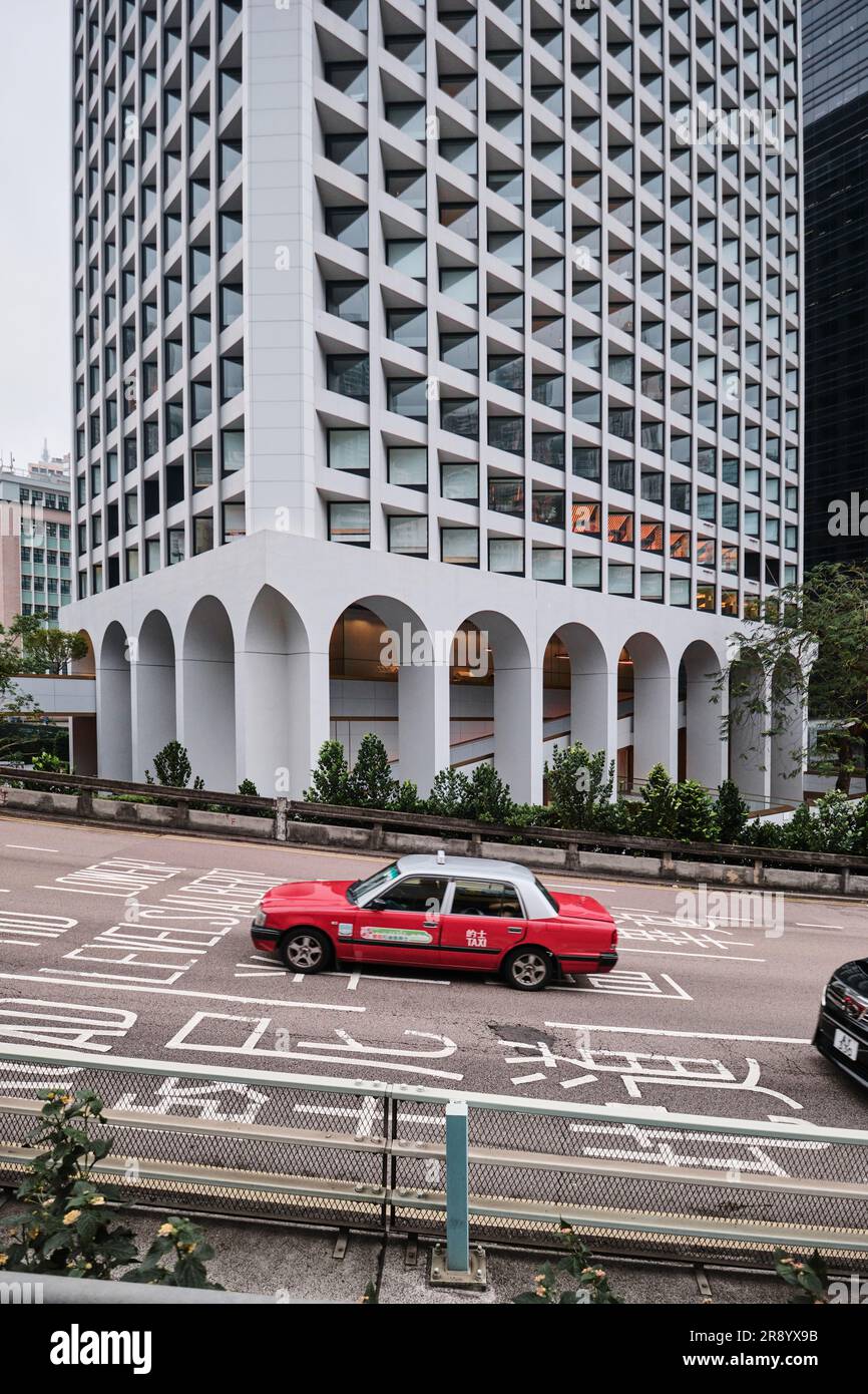 Hong Kong, Cina - 24 aprile 2023: The Murray Hotel, con un taxi rosso che passa in primo piano Foto Stock