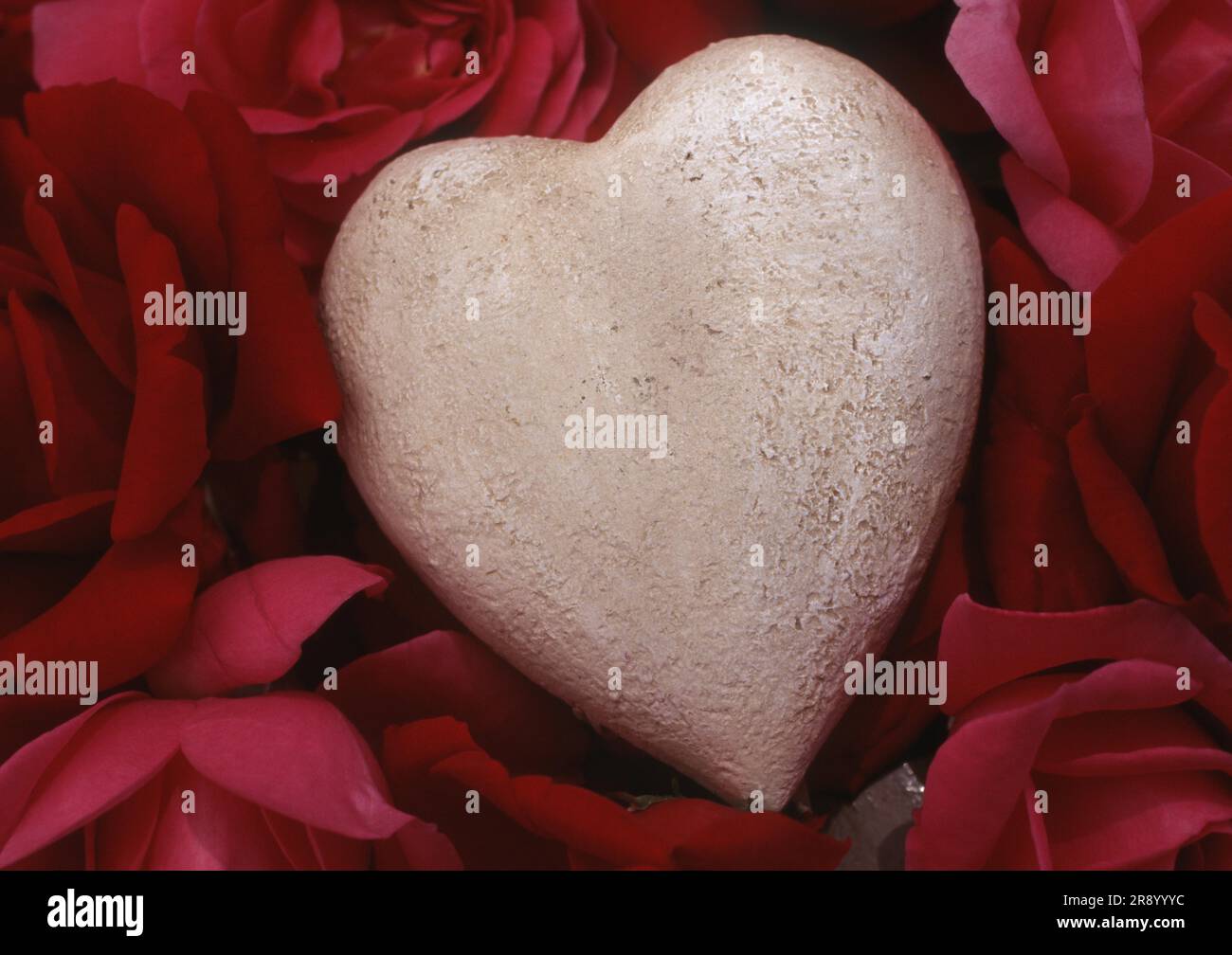 Stone Heart su Red Rose Petals, Heart, Love, Love Sorrow, Concept, Matrimonio, proposta di matrimonio, confessione d'amore, simbolo d'amore, Heartache Foto Stock