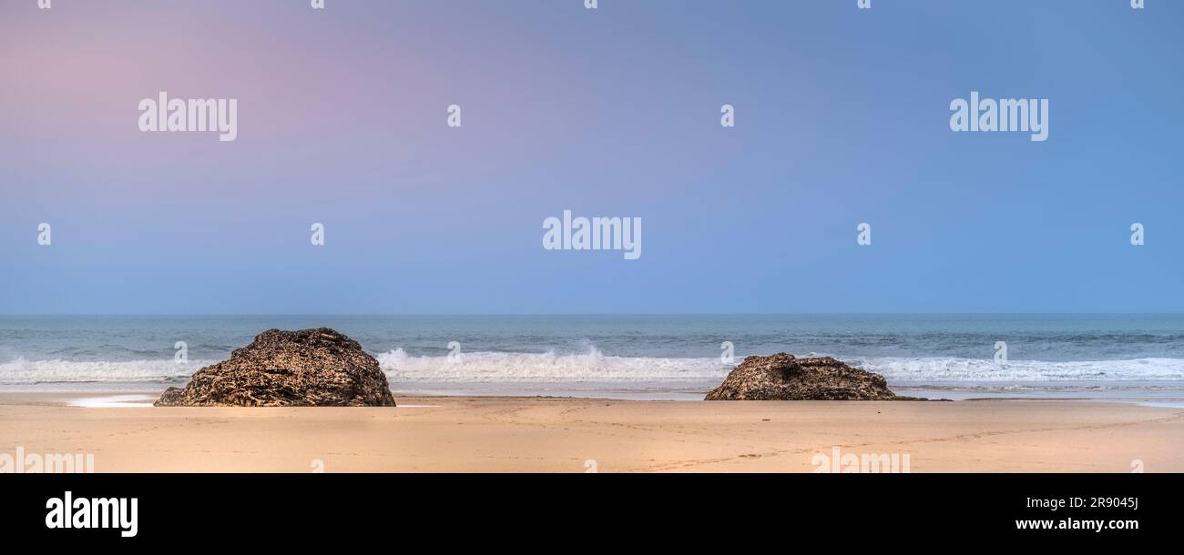 Un'immagine panoramica della luce notturna su due affioramenti rocciosi su una deserta spiaggia di Mawgan Porth in Cornovaglia, nel Regno Unito. Foto Stock