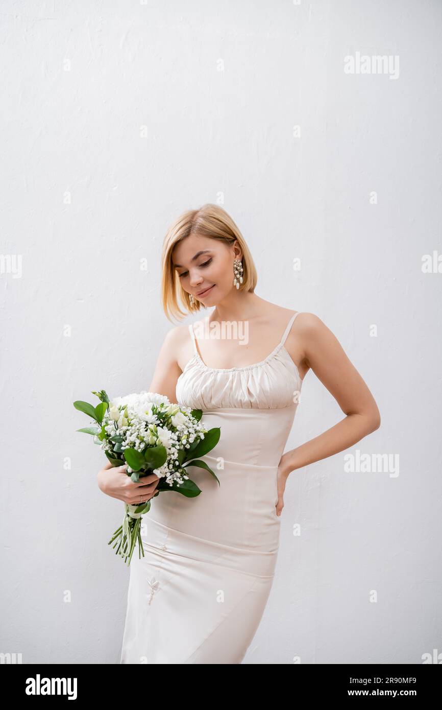 sposa felice e bionda in abito da sposa con bouquet su sfondo grigio, fiori bianchi, accessori da sposa, felicità, occasione speciale, beautifu Foto Stock