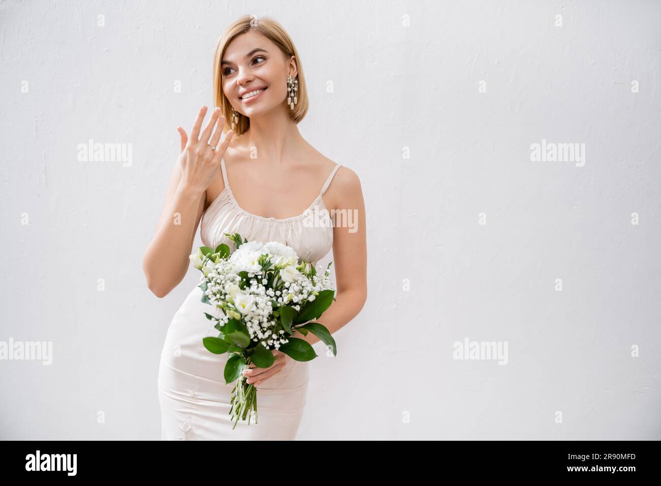 tema del matrimonio, splendida sposa bionda in abito da sposa con bouquet e anello di fidanzamento, fiori bianchi, accessori da sposa, felicità, grigio Foto Stock