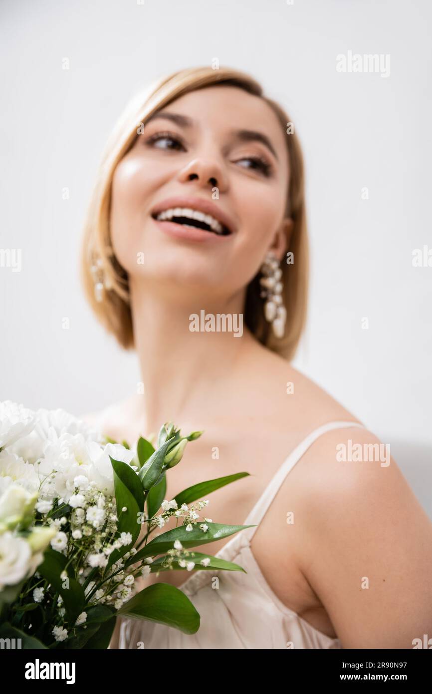 occasione speciale, bella sposa bionda in abito da sposa con bouquet su sfondo grigio, fiori bianchi, accessori da sposa, felicità, femminile, Foto Stock
