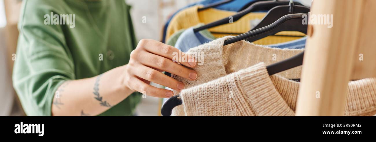 vista parziale di donne giovani e tatuate che smistano vestiti mentre si trovano in piedi vicino a scaffali con appendiabiti a casa, consapevole decluttering, moda sostenibile Foto Stock