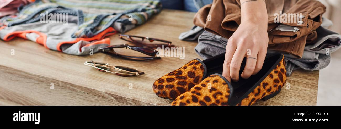 vista parziale di una donna che indossa scarpe con stampe di animali alla moda vicino agli occhiali da sole e ai vestiti prediletti sul tavolo a casa, scambi ecologici, sostenibile l Foto Stock