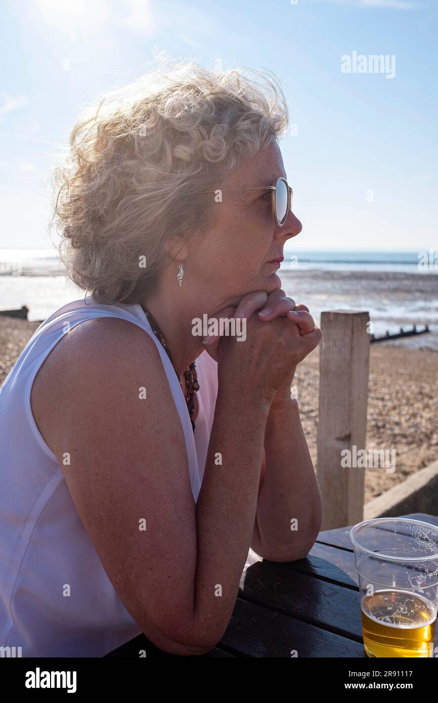 Whitstable North Kent , Inghilterra Regno Unito - la donna matura visitatrice sembra rilassata seduta al sole nel tardo pomeriggio in estate Foto Stock