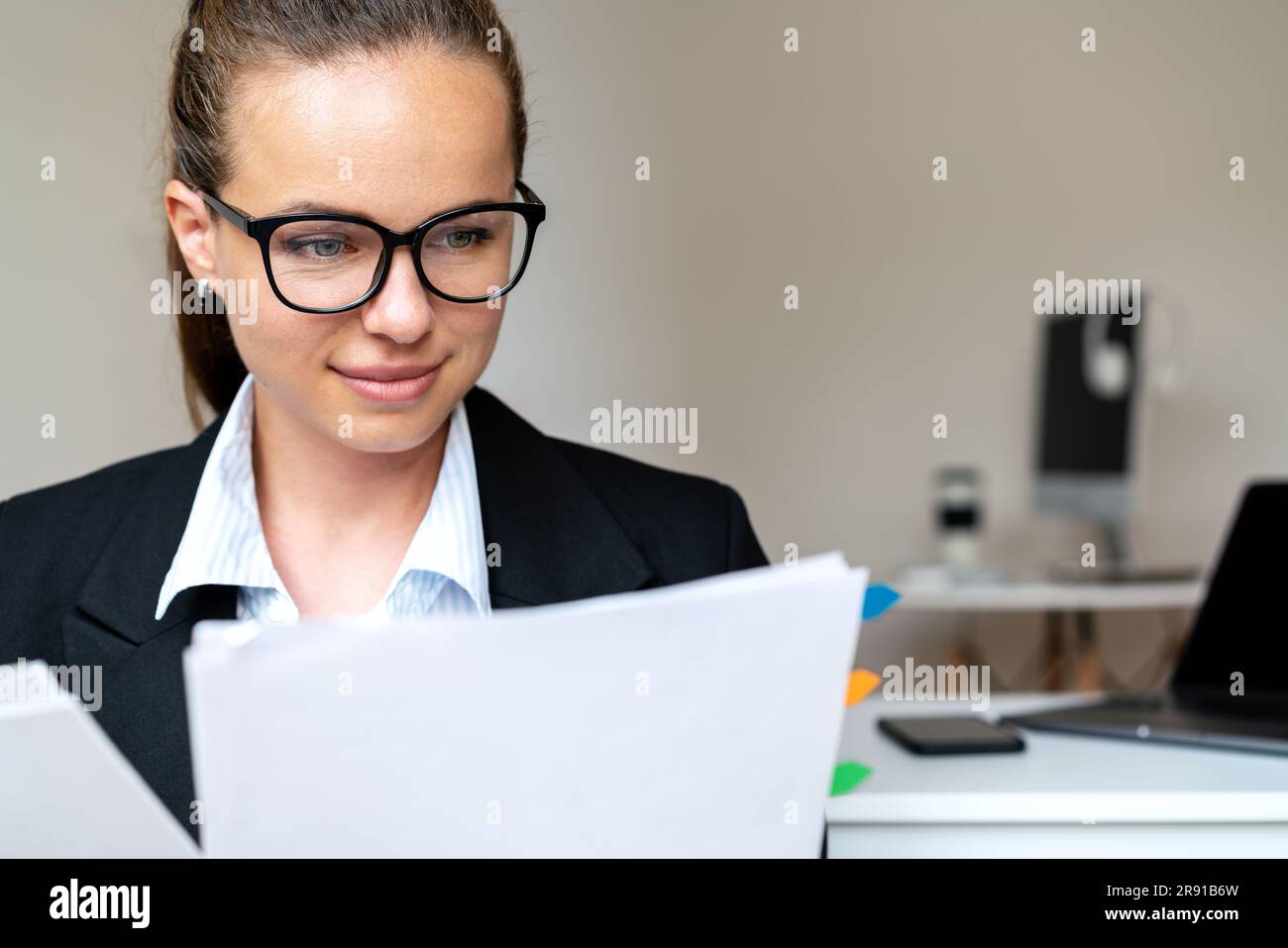 Donna bruna che indossa occhiali e abiti che lavora con documenti in ufficio. Foto Stock