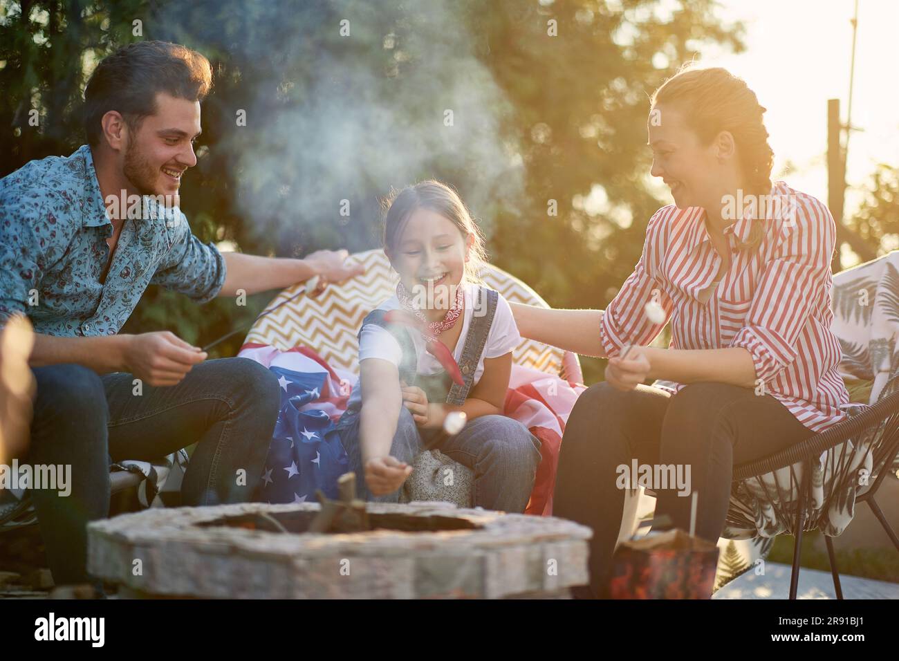 La famiglia si riunisce nel loro cortile, crogiolandosi nella gioia di stare insieme. I genitori e la loro figlia sono visti indulgere nel semplice piacere di roas Foto Stock