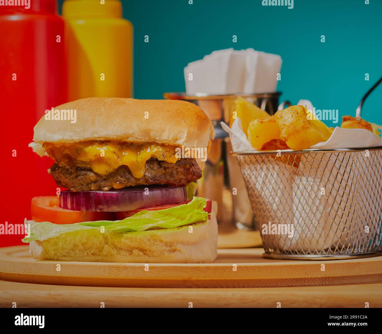 Hamburger al formaggio impilato con patatine fritte in un cestino con salse sullo sfondo in un ristorante di hamburger. Foto Stock