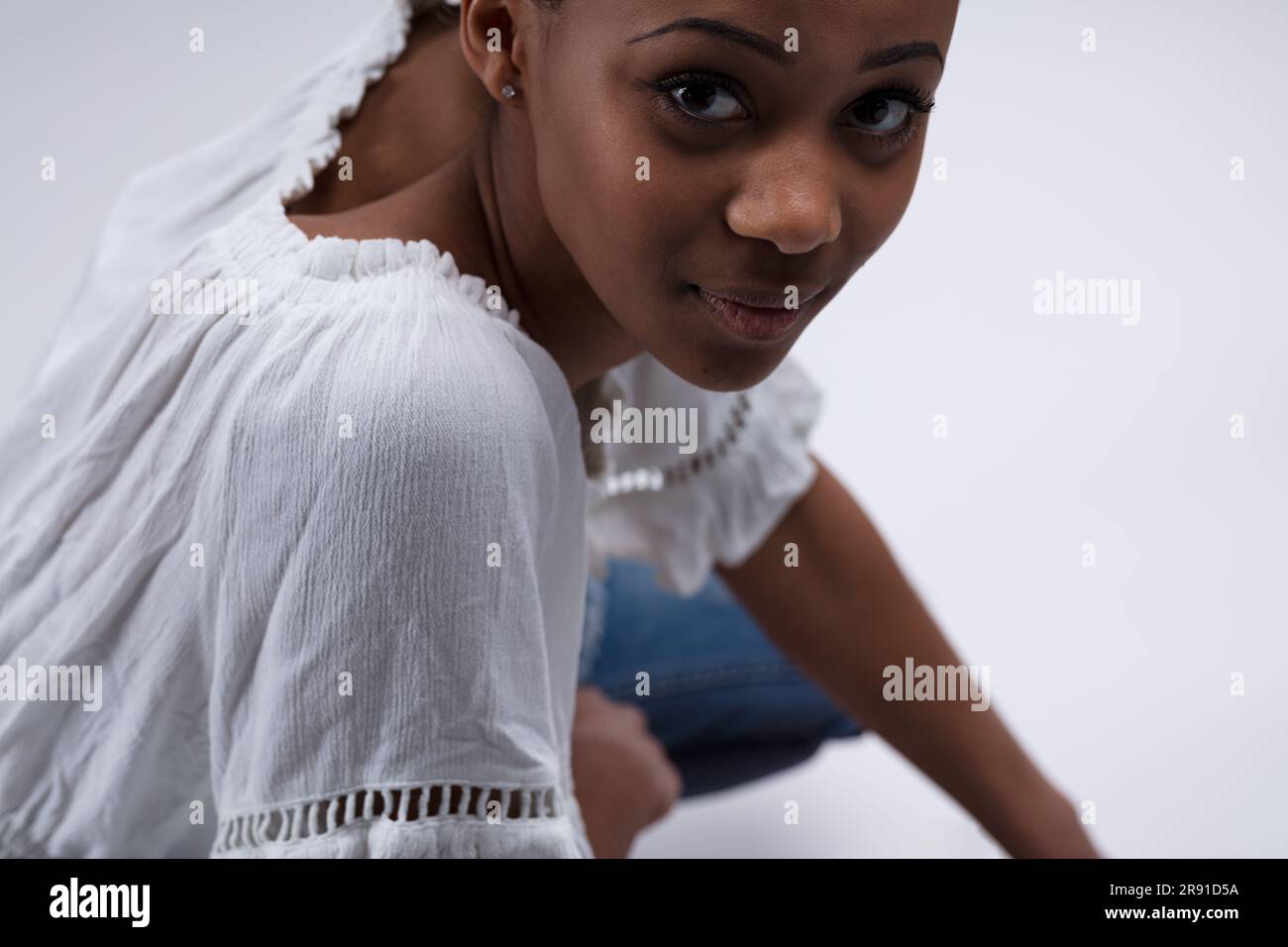 Ritratto da sotto di una giovane donna seduta, girandosi per ascoltare. Indossa una camicetta bianca e jeans, sembra curiosa se sei interessante o noiosa. SH Foto Stock