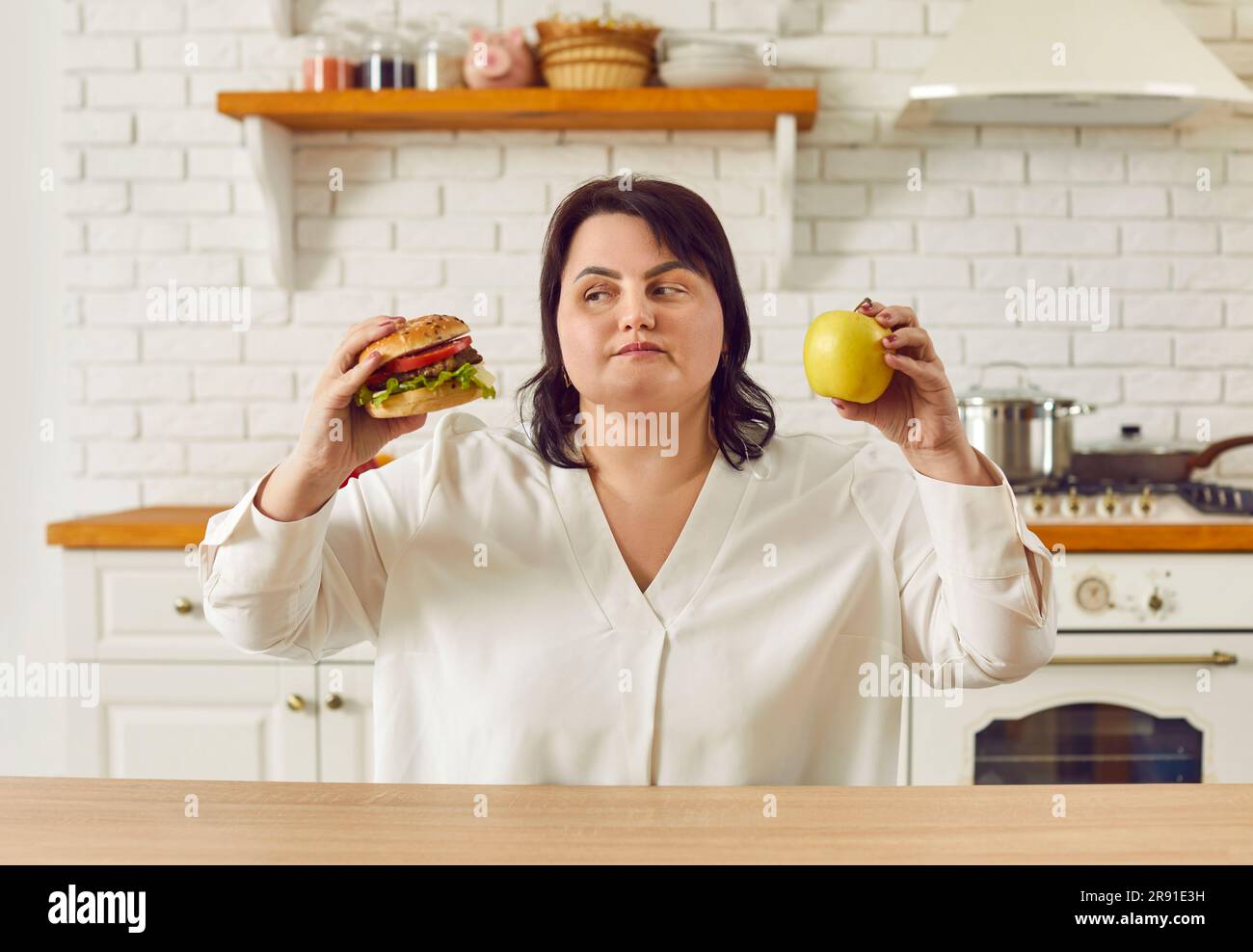 Donna in sovrappeso che tiene mela e hamburger e sceglie tra cibo sano e malsano Foto Stock