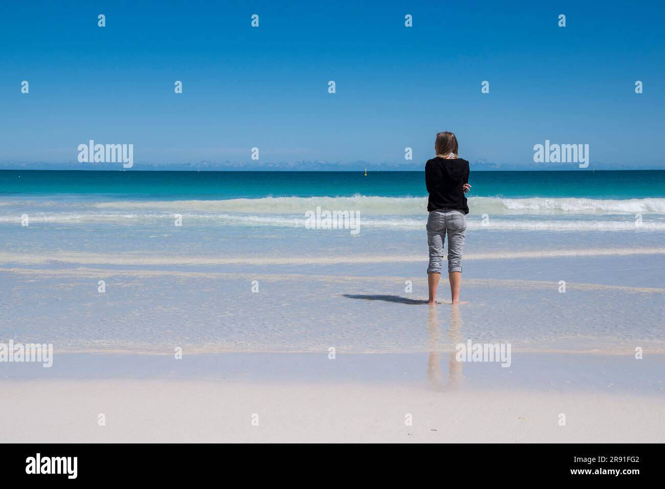 Una donna con i pantaloni arrotolati si gode l'acqua e la sabbia di Scarborough Beach a Perth, Australia Foto Stock