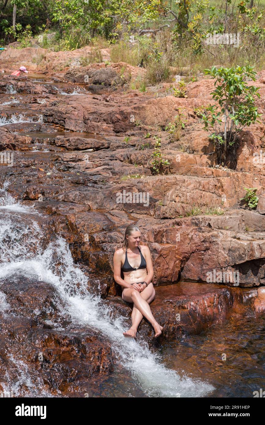 Una donna in bikini nero si rilassa al sole da una piccola cascata al buco di Buley Rock a Litchfield NP, nel Northern Territory in Australia Foto Stock